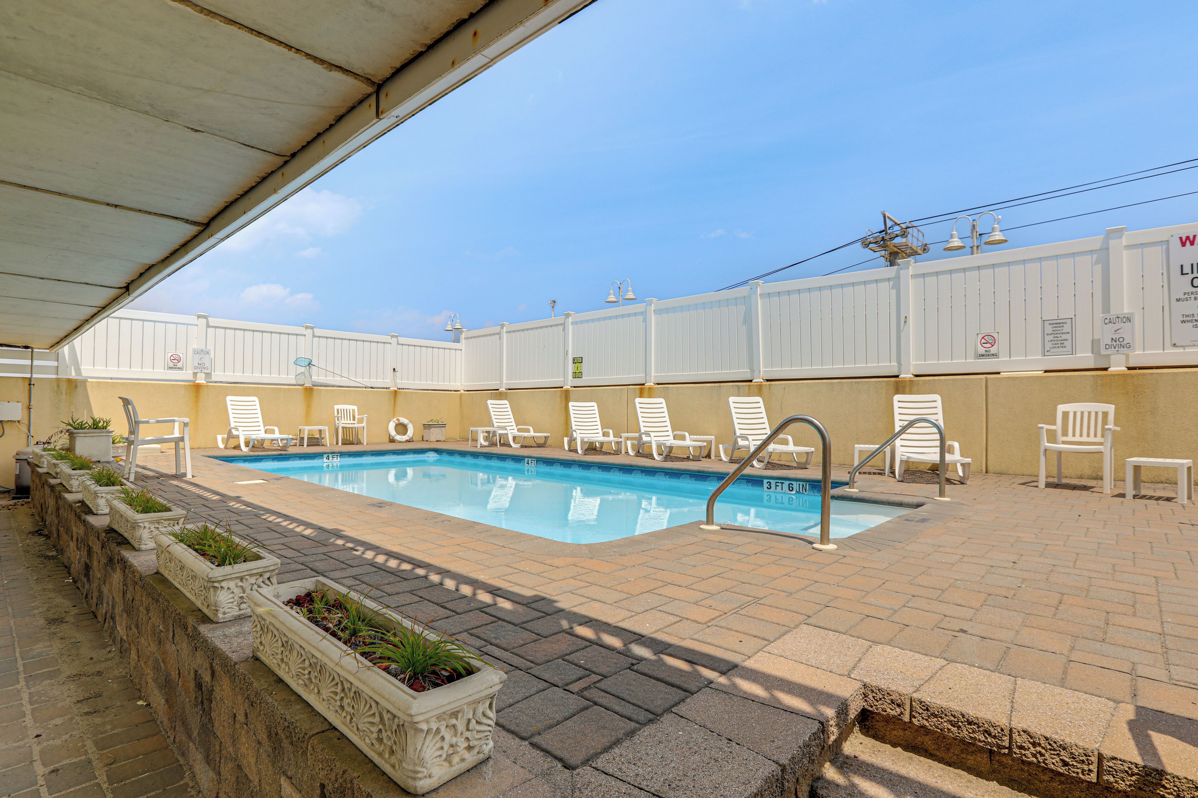 A swimming pool with lounge chairs, a covered area, and a white fence.