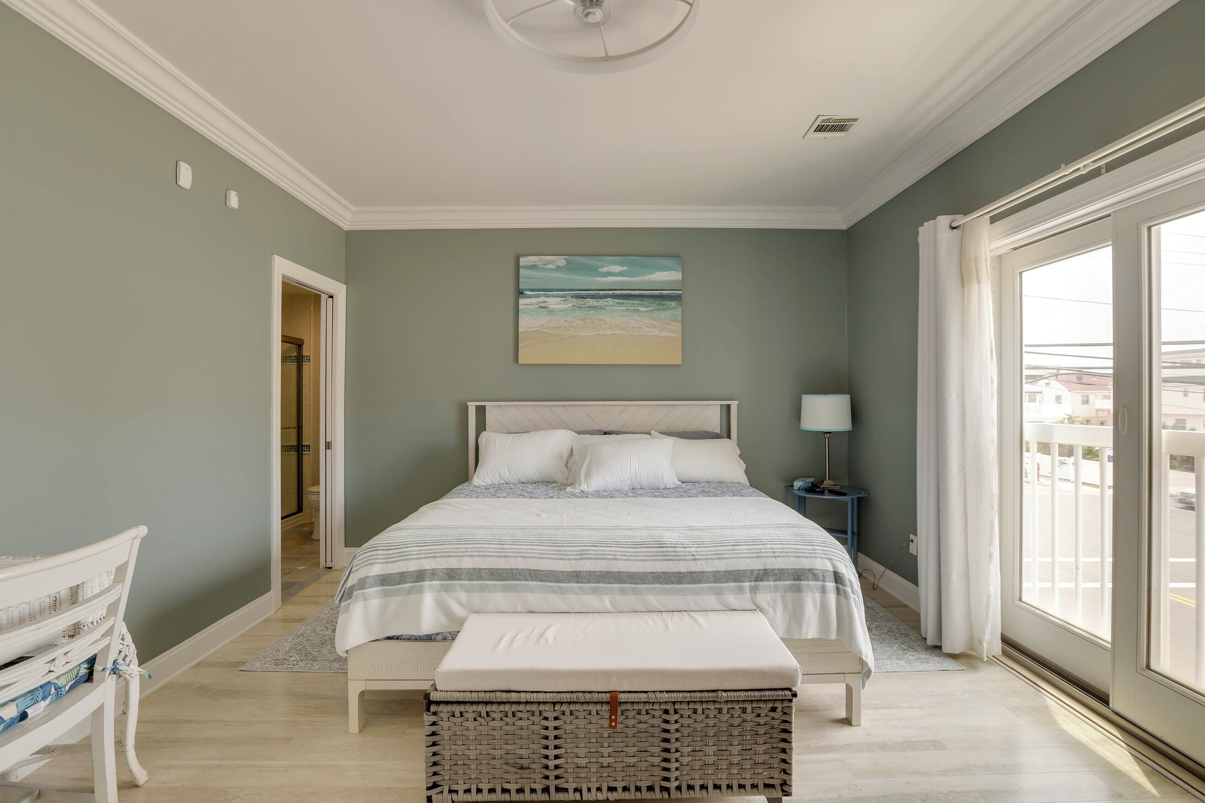 A bedroom with a bed, a bench, a nightstand, a lamp, and a painting of a beach.