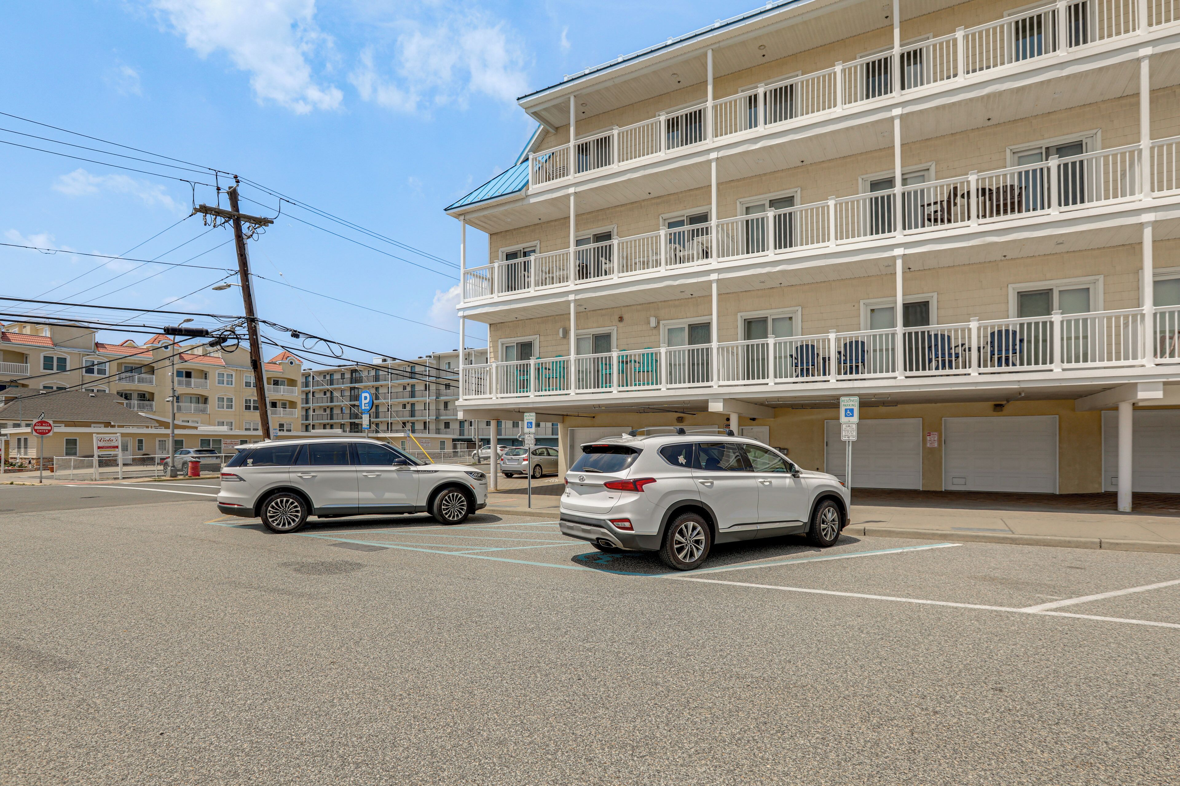 A multi-story building with balconies, a parking lot with two white SUVs, and a clear blue sky.
