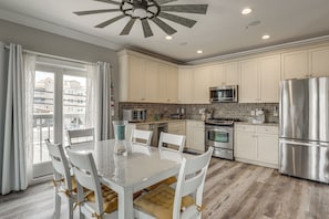 A modern kitchen with white cabinets, stainless steel appliances, and a dining area with white chairs and a table. - Premier Beachfront Location in Seaside Heights (Seaside Heights)