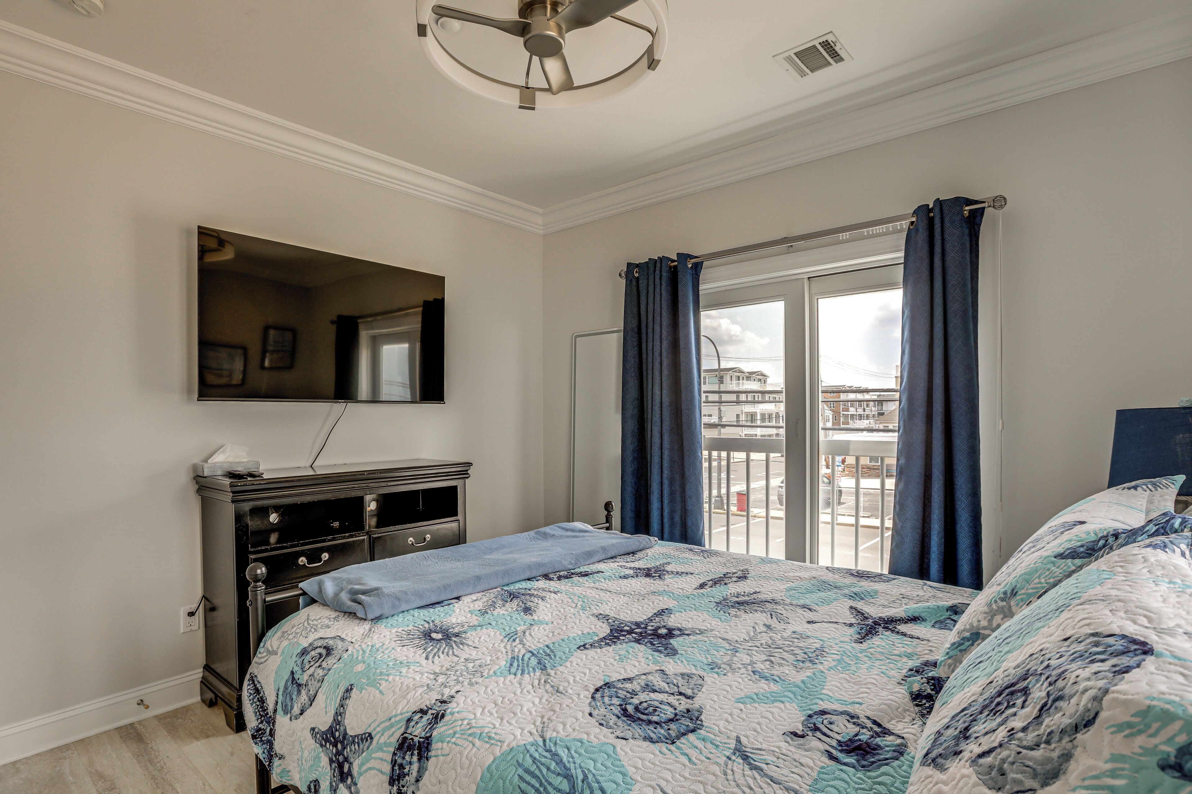 A bedroom with a bed, dresser, and a large window with curtains.