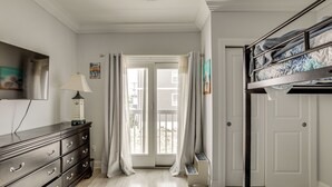 Ein Schlafzimmer mit Etagenbett, Kommode, Fernseher und einer Tür, die auf einen Balkon führt.