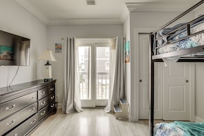 A bedroom with a bunk bed, a dresser, a television, and a door leading to a balcony. - Premier Beachfront Location in Seaside Heights (Seaside Heights)