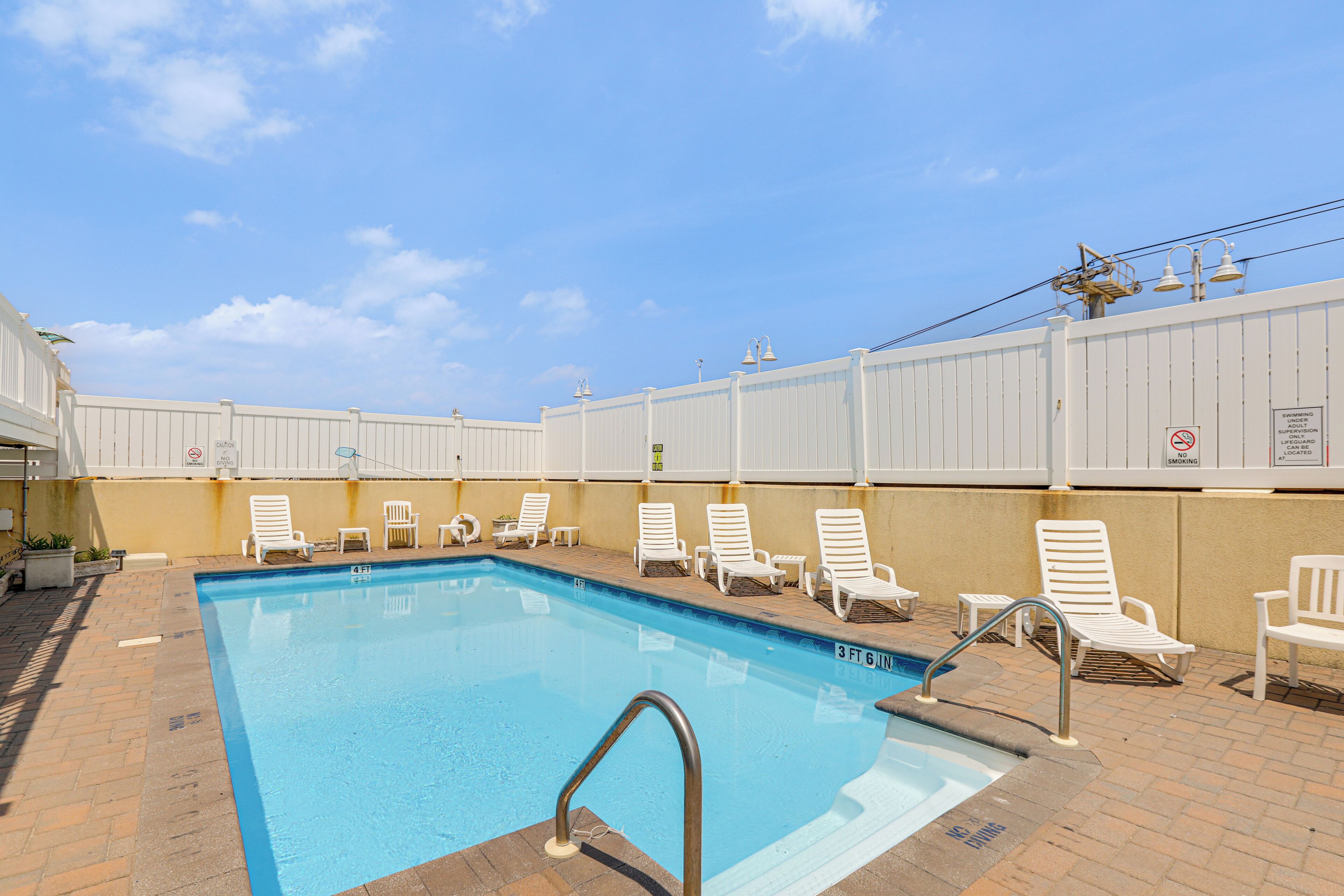 A swimming pool with a metal ladder, white lounge chairs, and a brick patio.