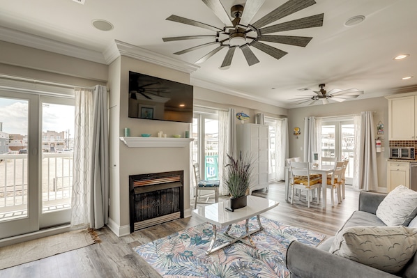 A spacious living area with a fireplace, ceiling fans, a dining table with chairs, and a view through large windows. - Premier Beachfront Location in Seaside Heights (Seaside Heights)