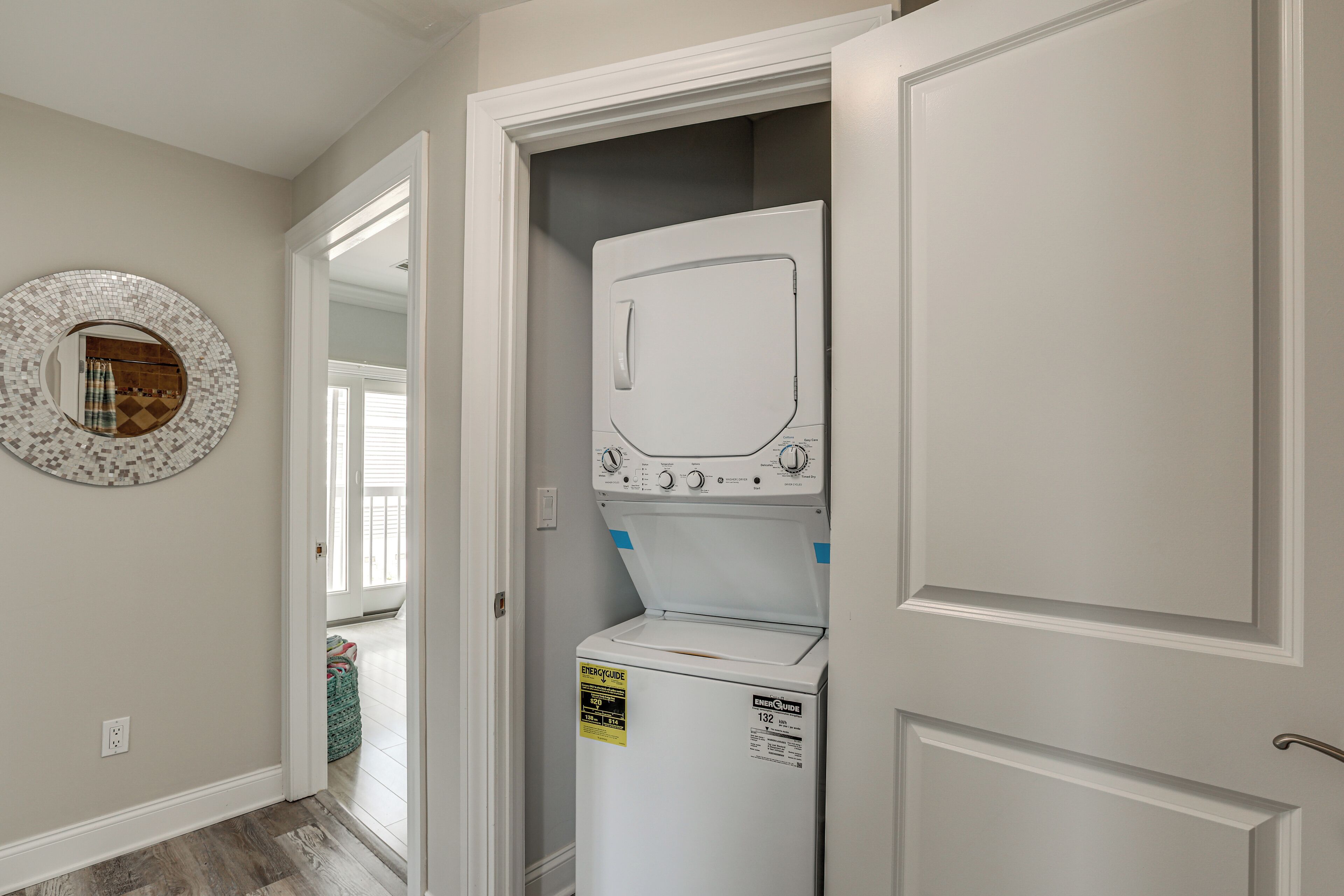 A laundry room with a front-loading washer and dryer, a door leading to another room, and a wall-mounted mirror.