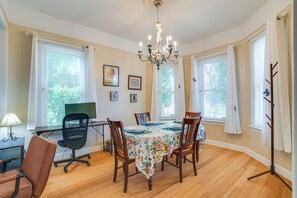 Ein Esszimmer mit einem für sechs Personen gedeckten Tisch, einer Chandelierleuchtre und großen Fenstern mit Jalousien.