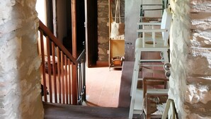 Un escalier rustique mène à une pièce dont le plafond est en bois, qui contient une chaise en bois et une étagère sur laquelle sont disposés divers objets.