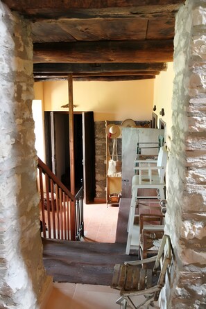 Una escalera rústica que lleva a una habitación con techo de madera, una silla de madera y un estante con diversos objetos.