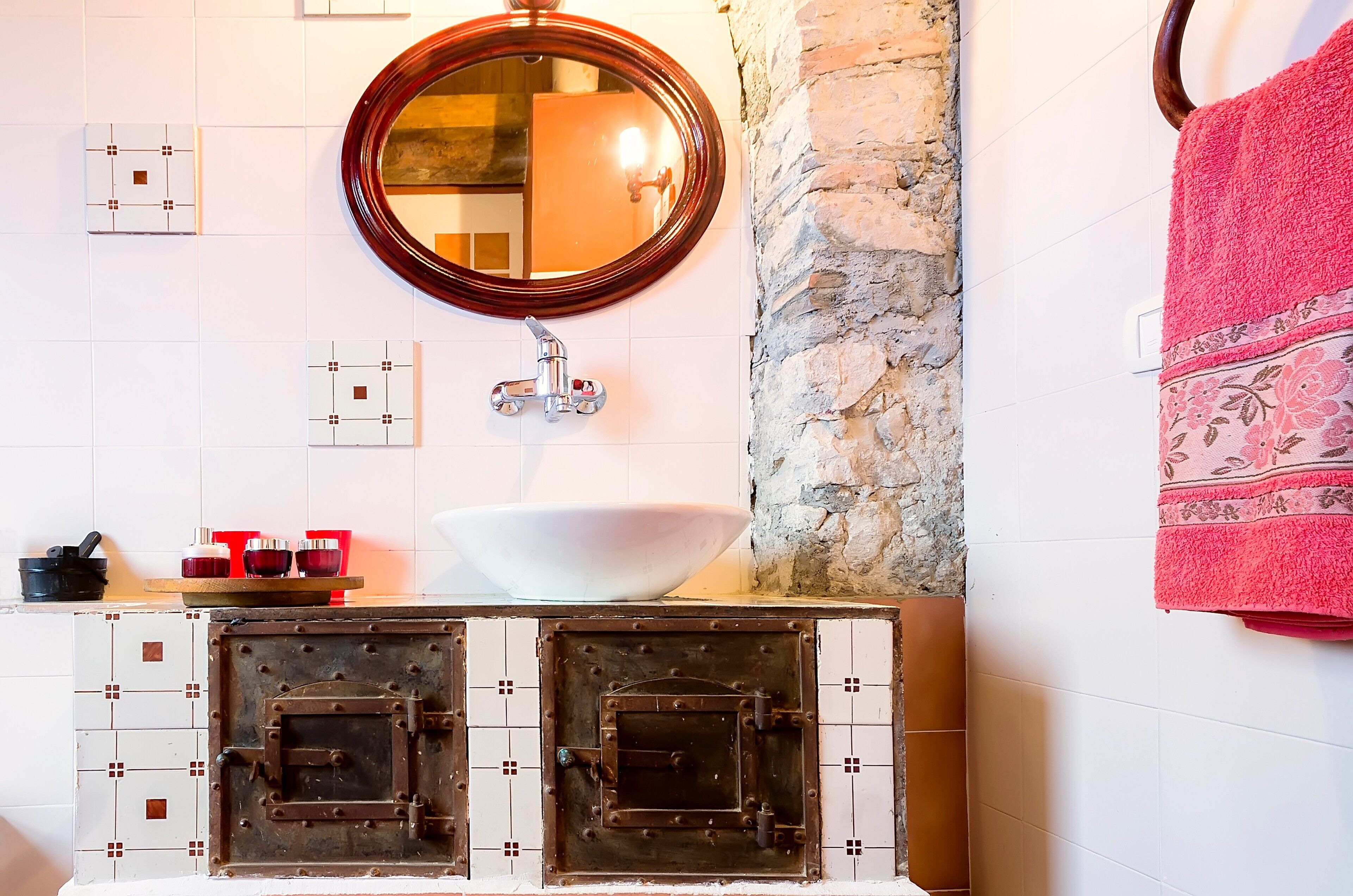 A bathroom with a white sink, a large mirror, a stone wall, and a red towel.