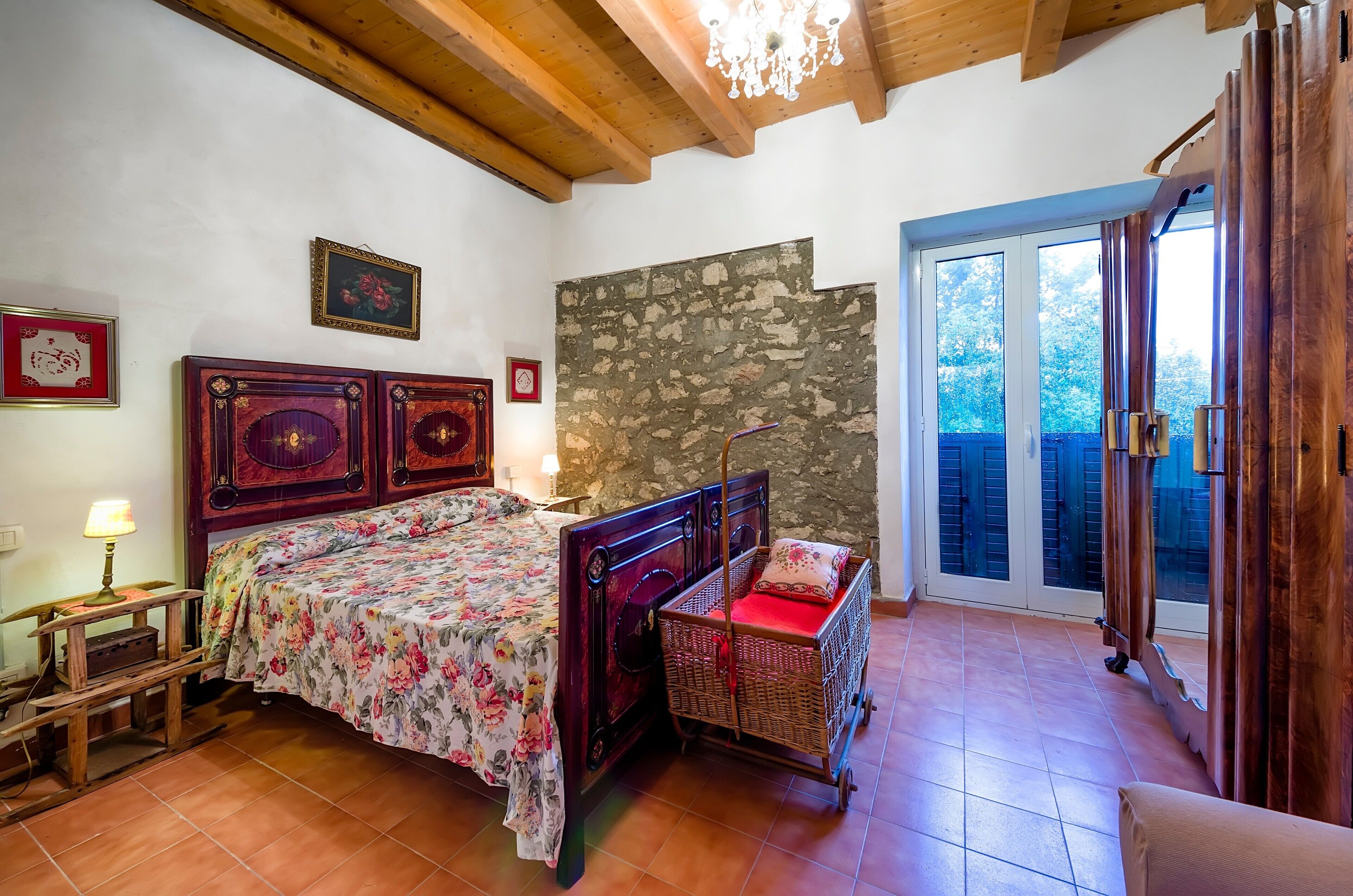 A bedroom with a wooden bed, a stone wall, a wicker basket, and a view through a glass door.