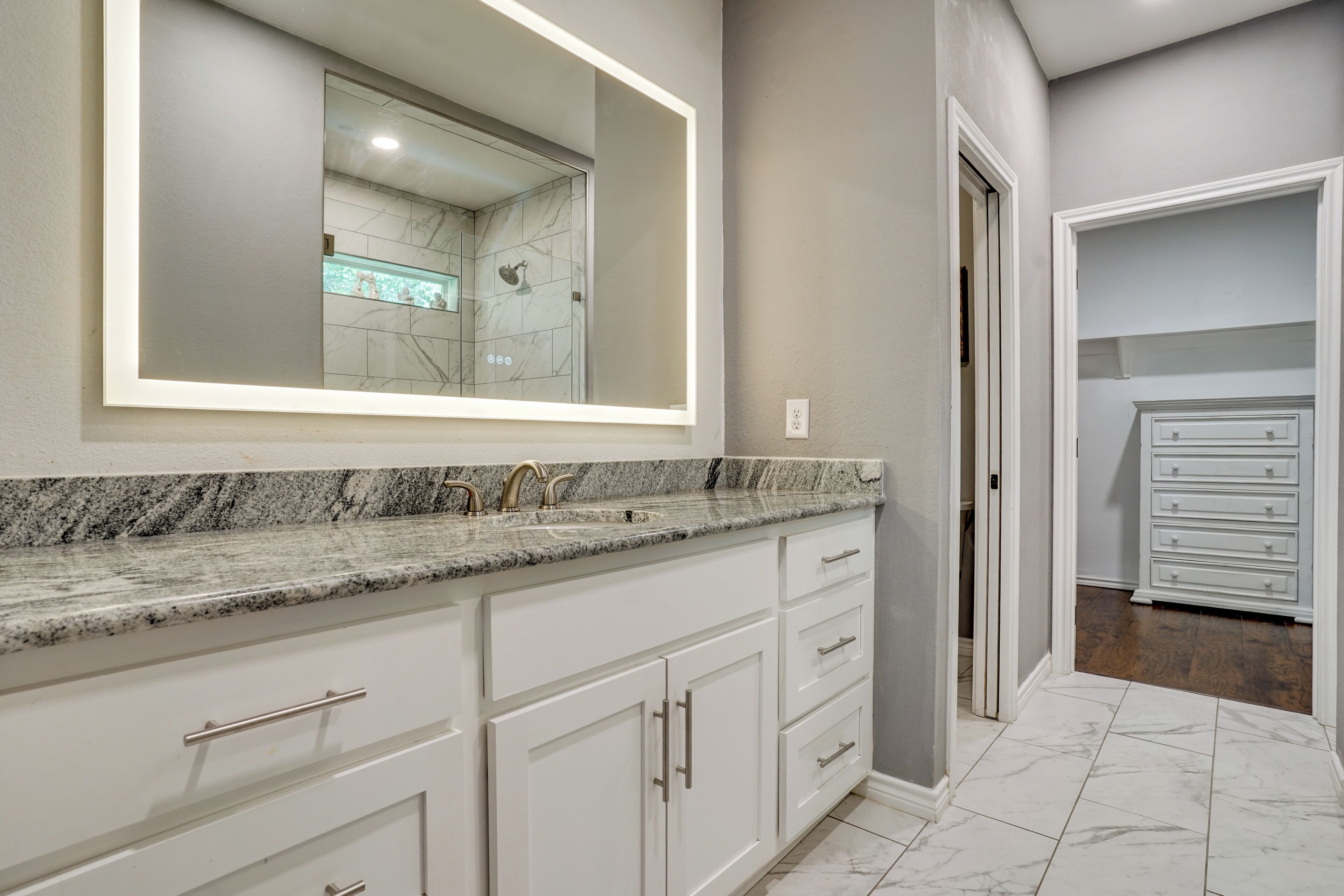A bathroom with a large mirror, marble countertop, and white cabinetry.