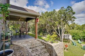 Ein überdachter Patio-Bereich mit Deckenventilator, Gartenmöbeln und einer Steinwand.