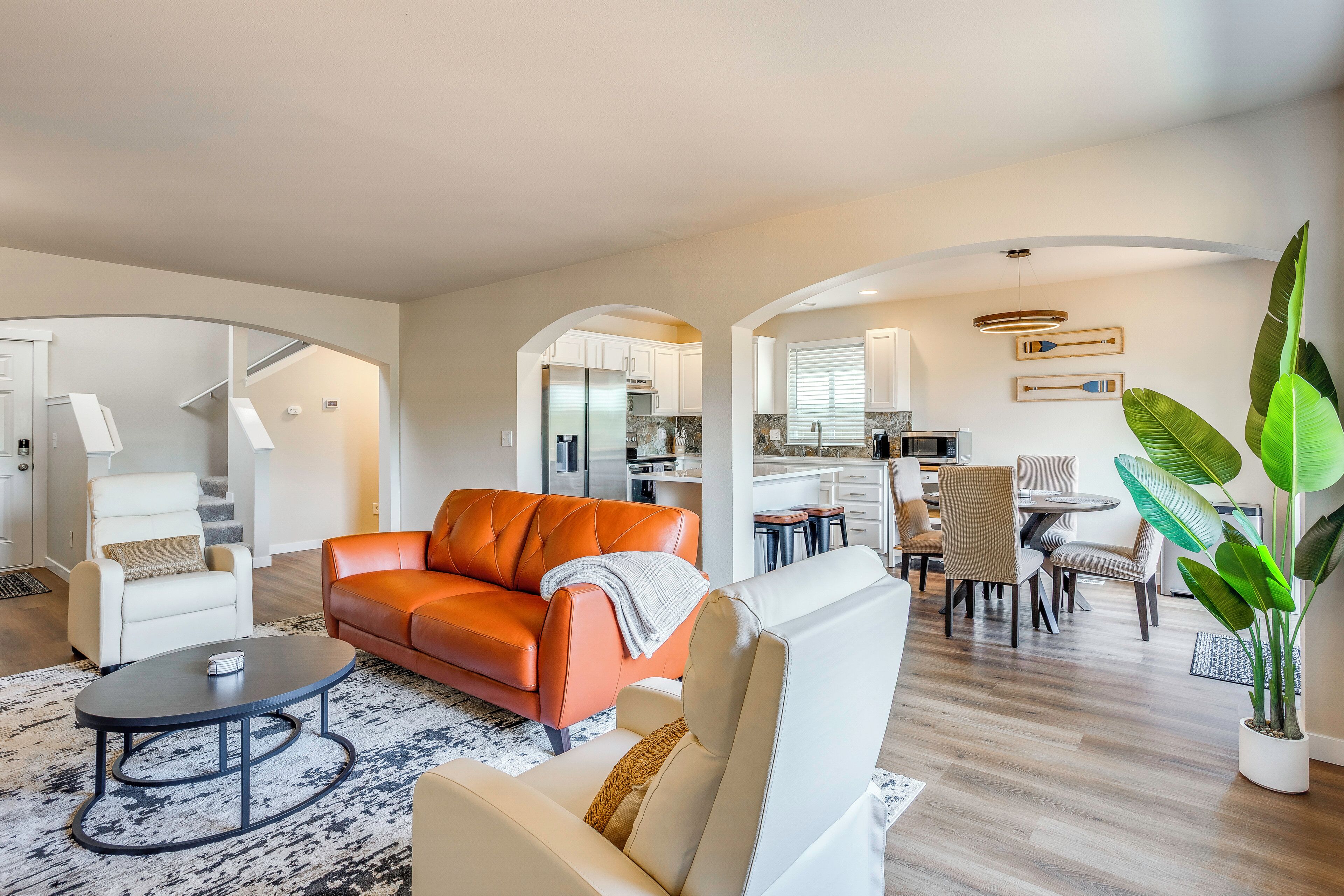 A modern living room with a sofa, armchair, coffee table, and a dining area with chairs and a table.