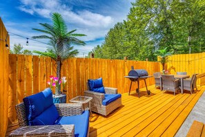 An outdoor deck with wicker furniture, a grill, and a wooden fence.