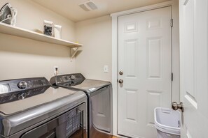 A laundry room with a front-loading washer and dryer, a shelf above, and a white door. - 10 Min to Fairgrounds! Family Retreat in Puyallup (Puyallup)