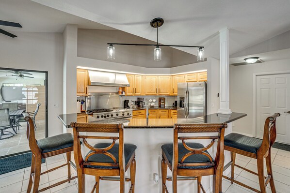 A modern kitchen with wooden cabinets, a central island, and a dining area with wooden chairs. - Luxury Oasis w/ Pool, Hot Tub, Dock & Sauna (Port Charlotte)