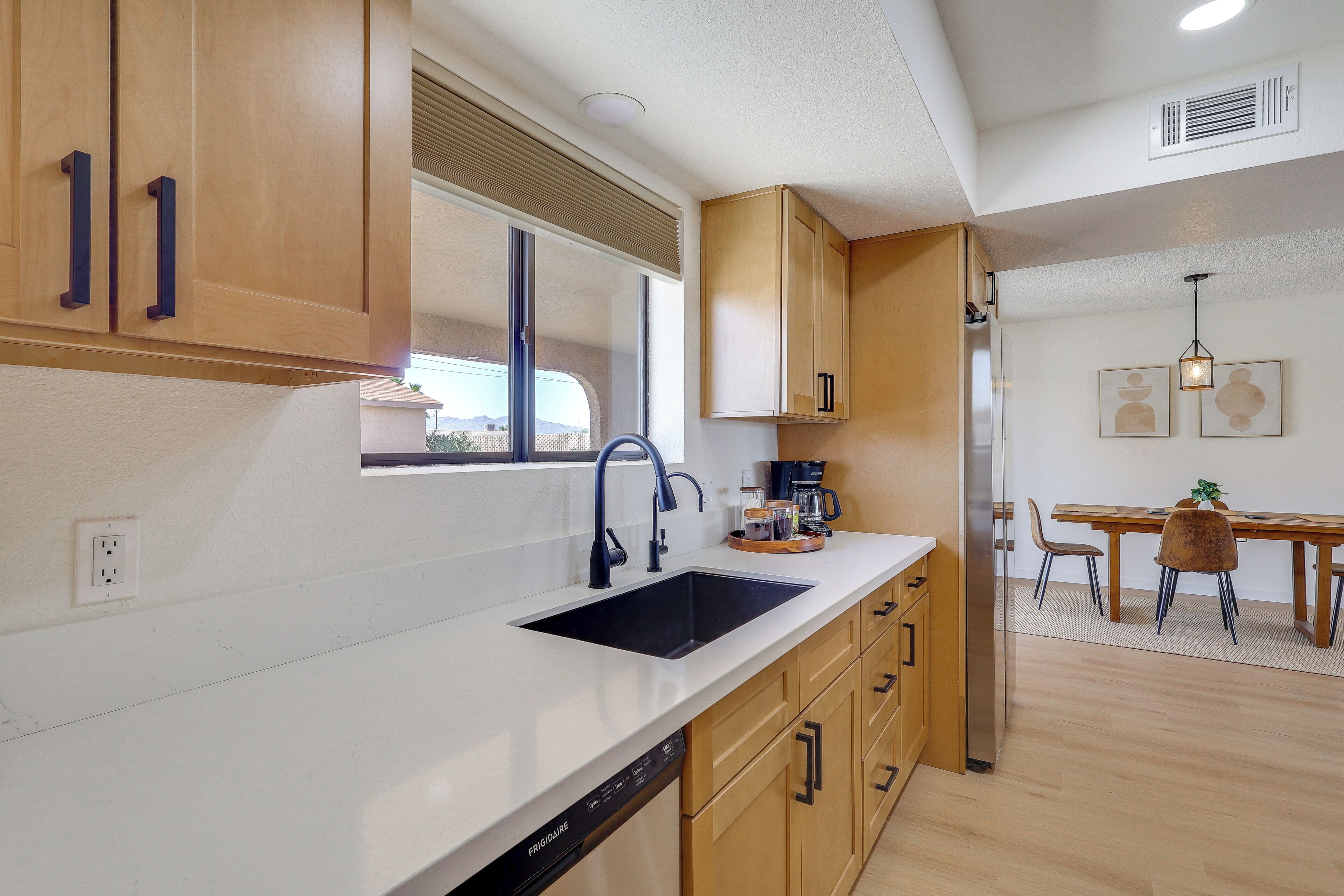 Una cocina moderna con lavavajillas, pileta, armarios de madera y un comedor con sillas y mesa.