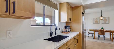 Una cocina moderna con lavavajillas, pileta, armarios de madera y un comedor con sillas y mesa.