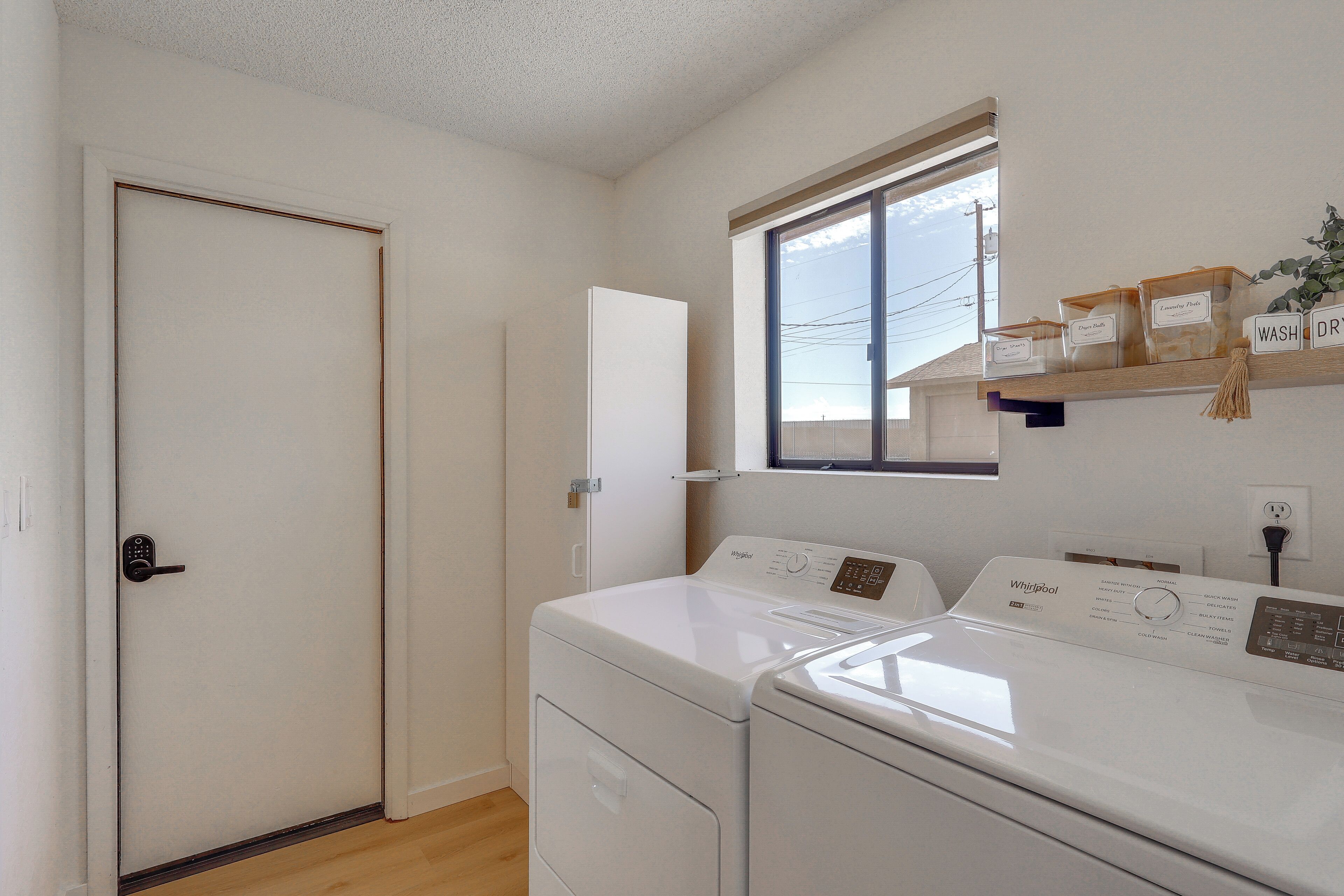 Un cuarto de lavandería con lavadora y secadora, una ventana y un estante con recipientes etiquetados.