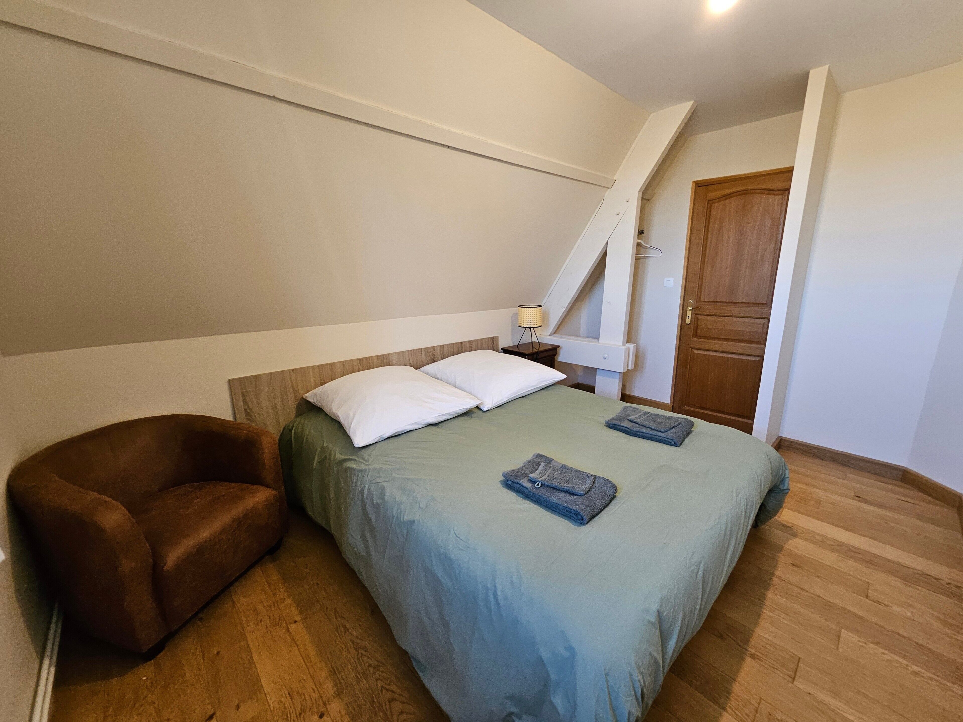 A bedroom with a bed, a chair, a nightstand, and a wooden door.