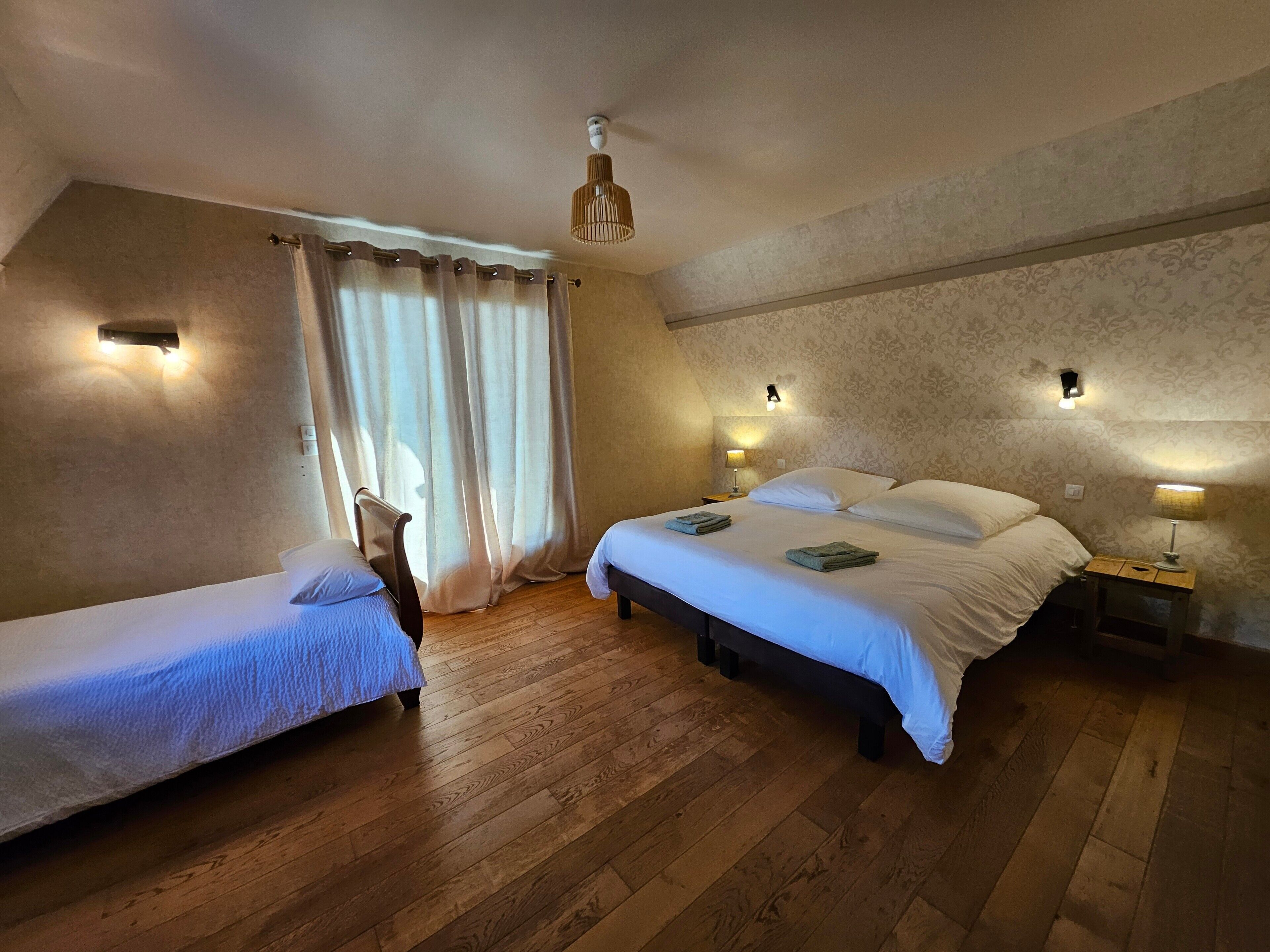 A room with two beds, wooden flooring, a ceiling fan, and wall-mounted lamps.