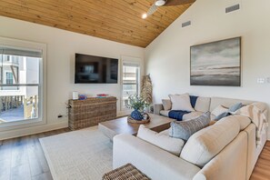 Uma sala de estar com teto de madeira, uma TV de tela plana, um quadro grande, um sofá e uma mesa lateral de vime.