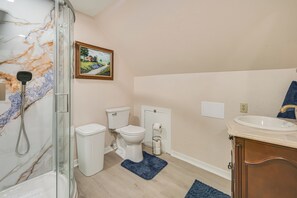 Un baño con cabina de ducha de vidrio, inodoro, lavabo y alfombra azul.