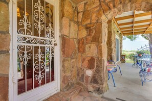 A stone building with a wrought iron gate, a covered patio with outdoor furniture, and a view of the surrounding landscape.
