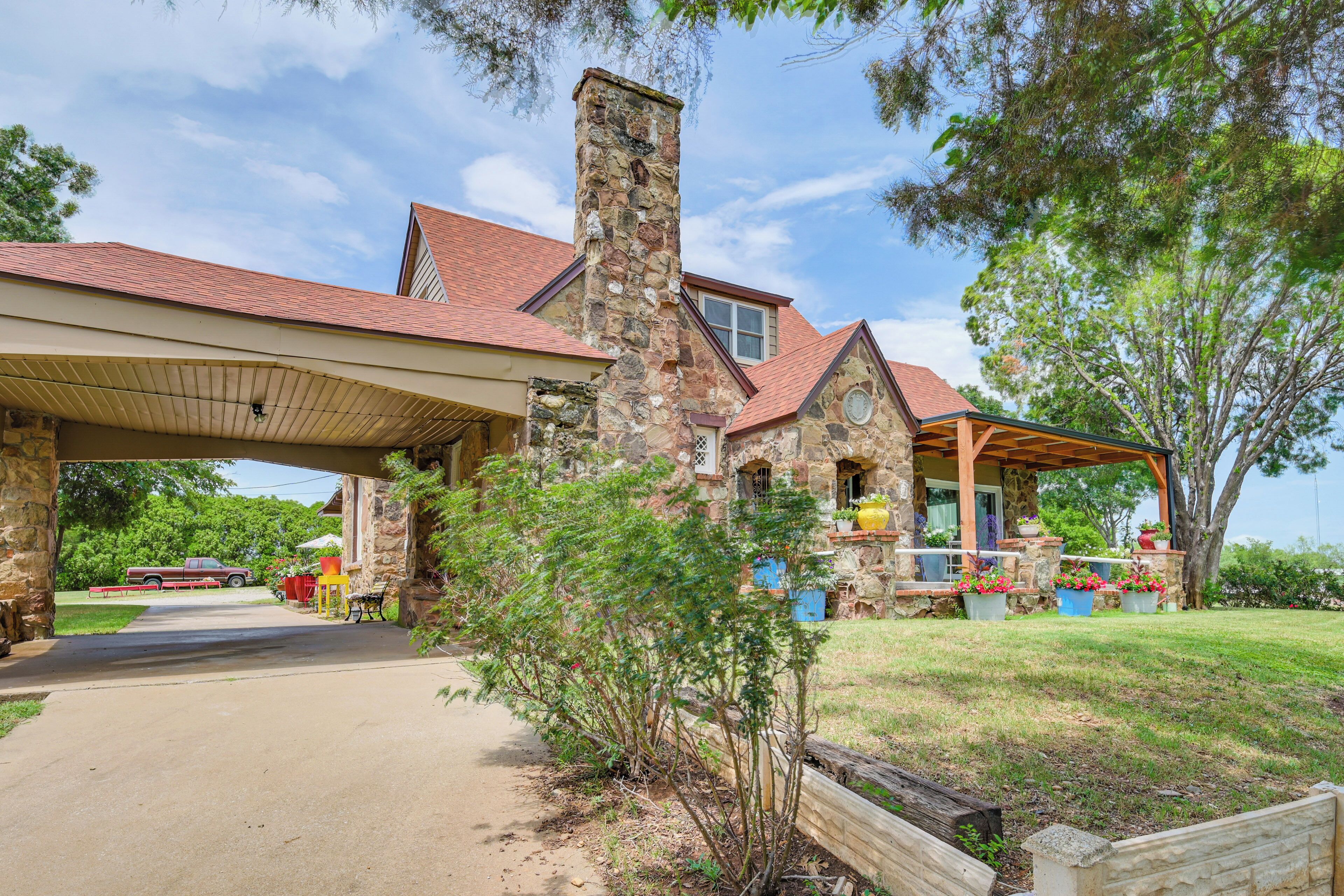 A stone house with a covered porch, a chimney, and a driveway leading to a parked truck.