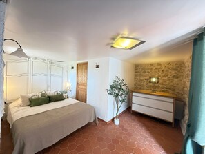 A bedroom with a bed, bedside lamp, wooden door, potted plant, and a dresser with drawers. - Apartment "L’échappée Provençale de Callian" with Mountain View, Wi-Fi, and Air Conditioning (Callian)