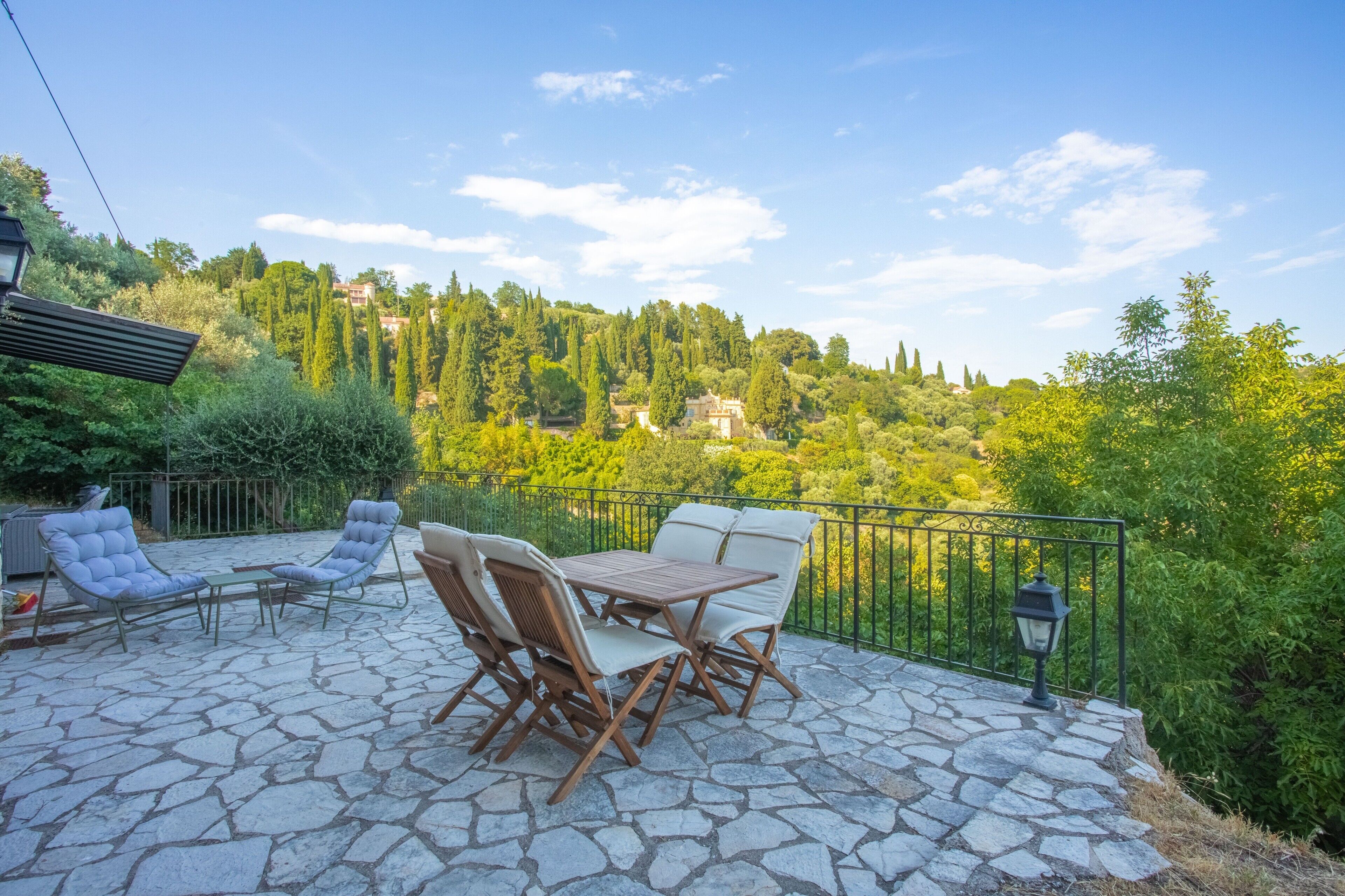A patio with stone flooring, outdoor furniture, and a view of a hill with trees and buildings.