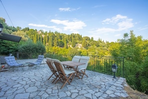A patio with stone flooring, outdoor furniture, and a view of a hill with trees and buildings.