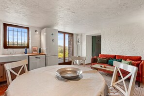A dining area with a table, chairs, a red couch, and a view through a window. - Apartment "L’échappée Provençale de Callian" with Mountain View, Wi-Fi, and Air Conditioning (Callian)