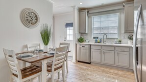 Une cuisine avec des meubles blancs, un réfrigérateur en acier inoxydable et un coin repas comprenant une table en bois et des chaises blanches.
