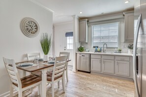 Une cuisine avec des meubles blancs, un réfrigérateur en acier inoxydable et un coin repas comprenant une table en bois et des chaises blanches.