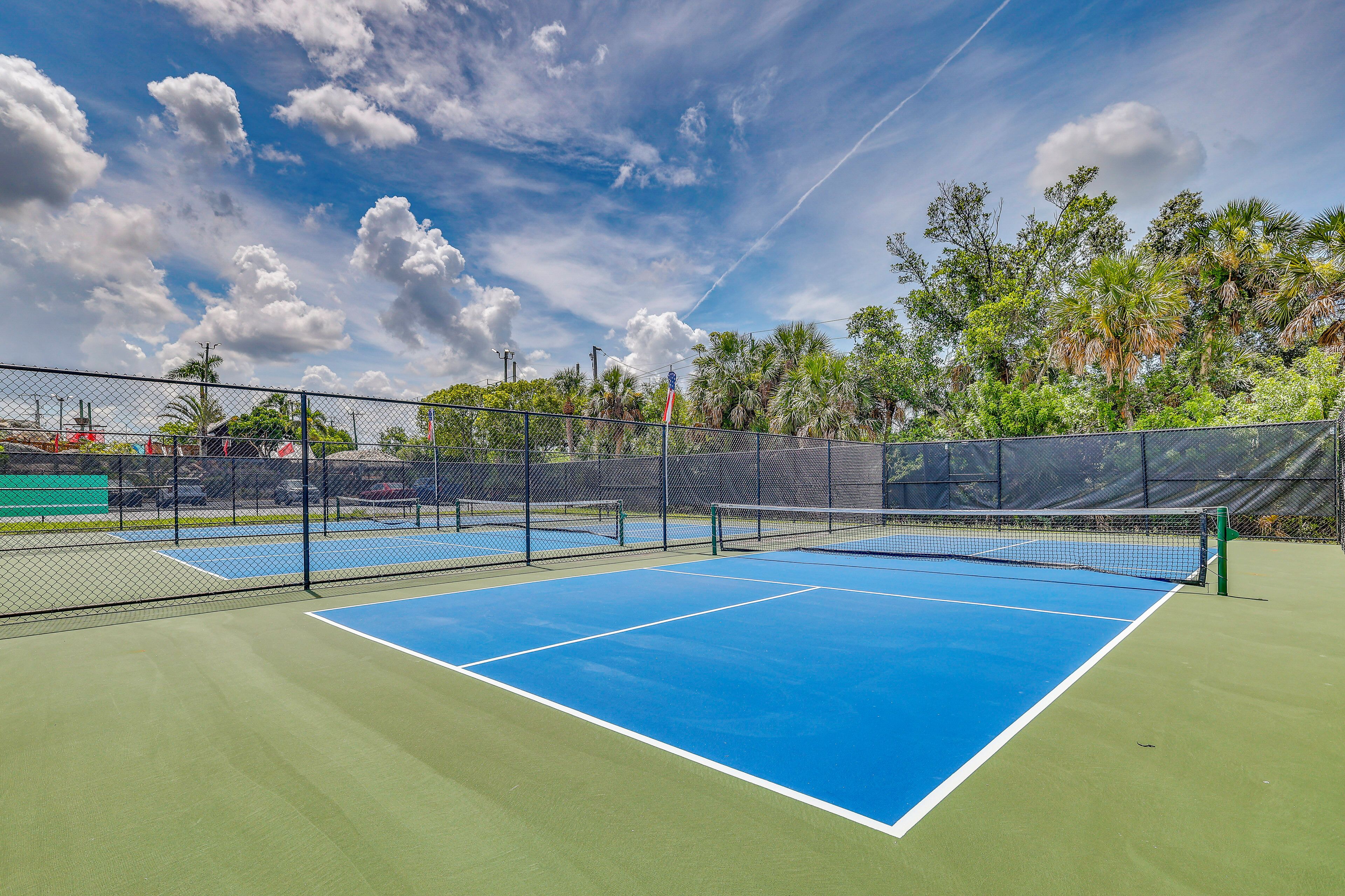Un court de tennis avec un filet, entouré d’une clôture et d’arbres.