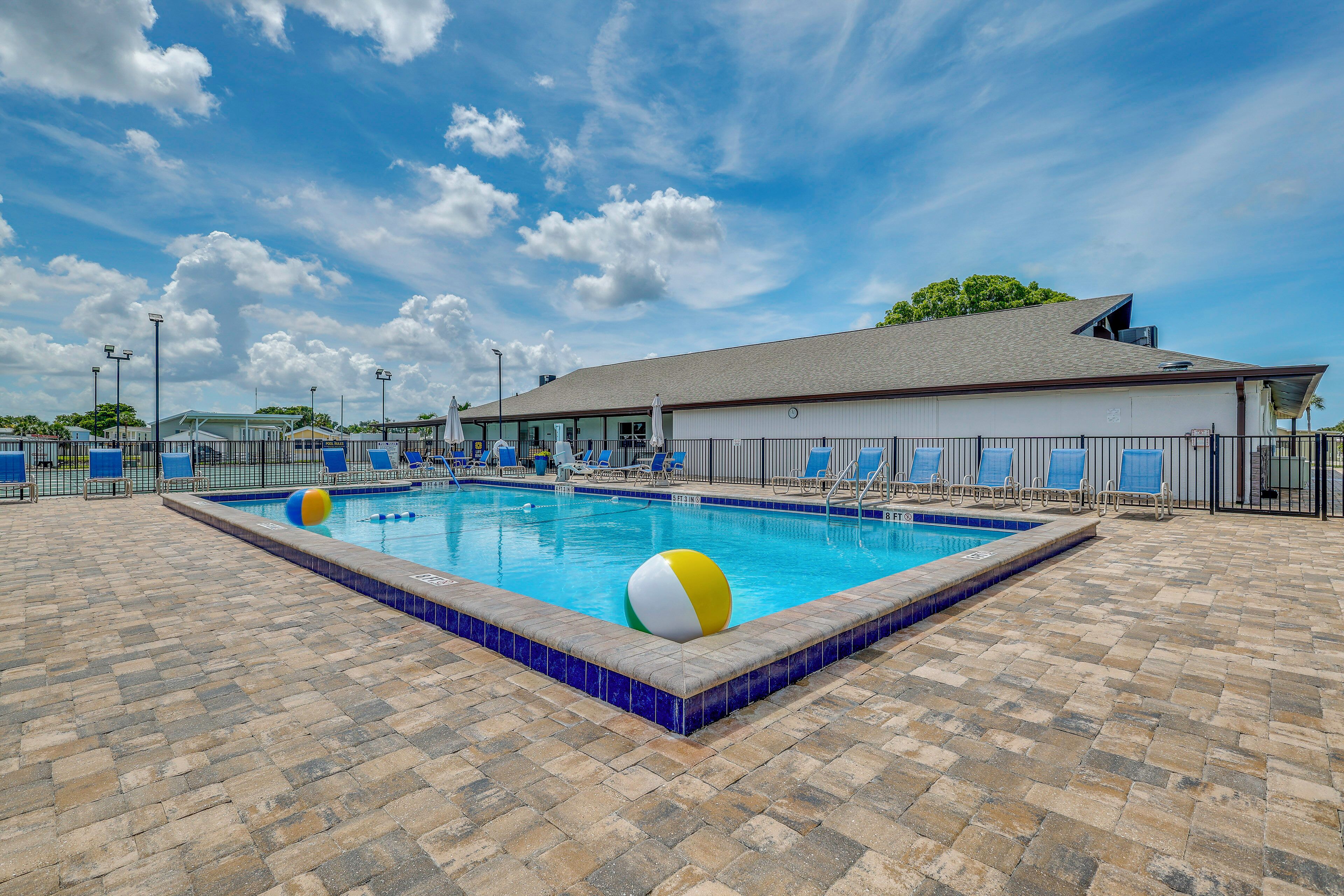A swimming pool with a tiled deck, lounge chairs, and a building in the background.