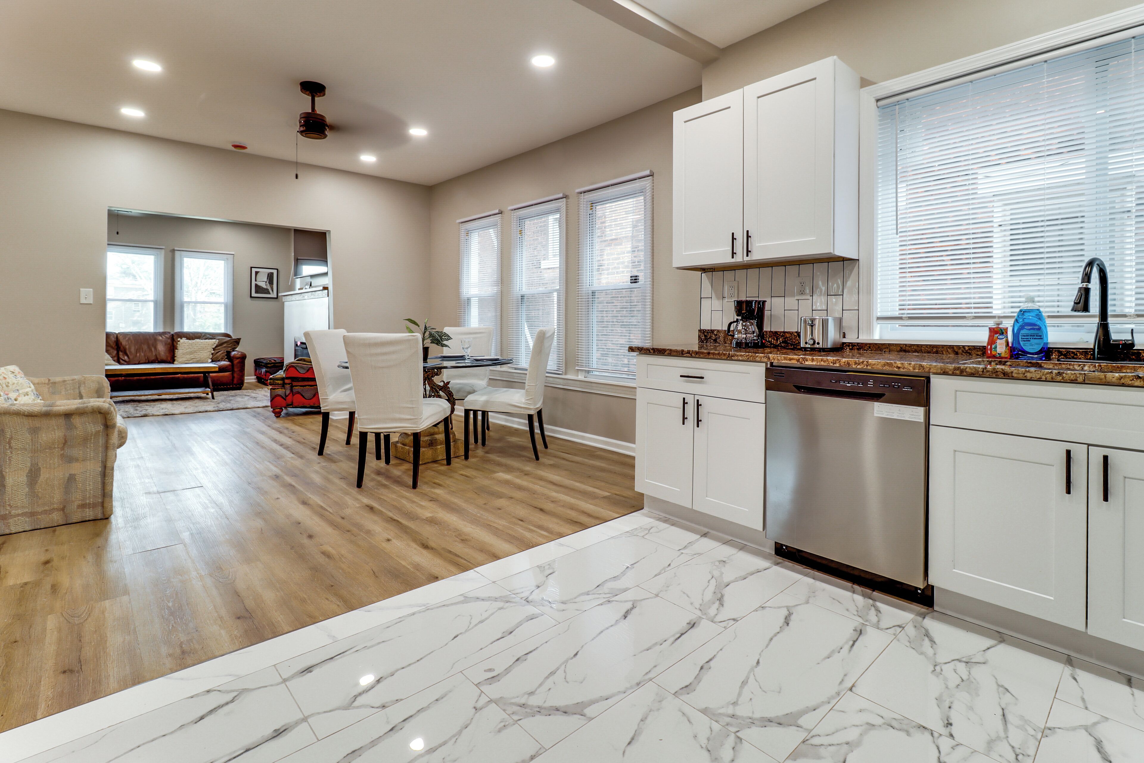 A modern kitchen with white cabinets, a marble countertop, and a built-in dishwasher.