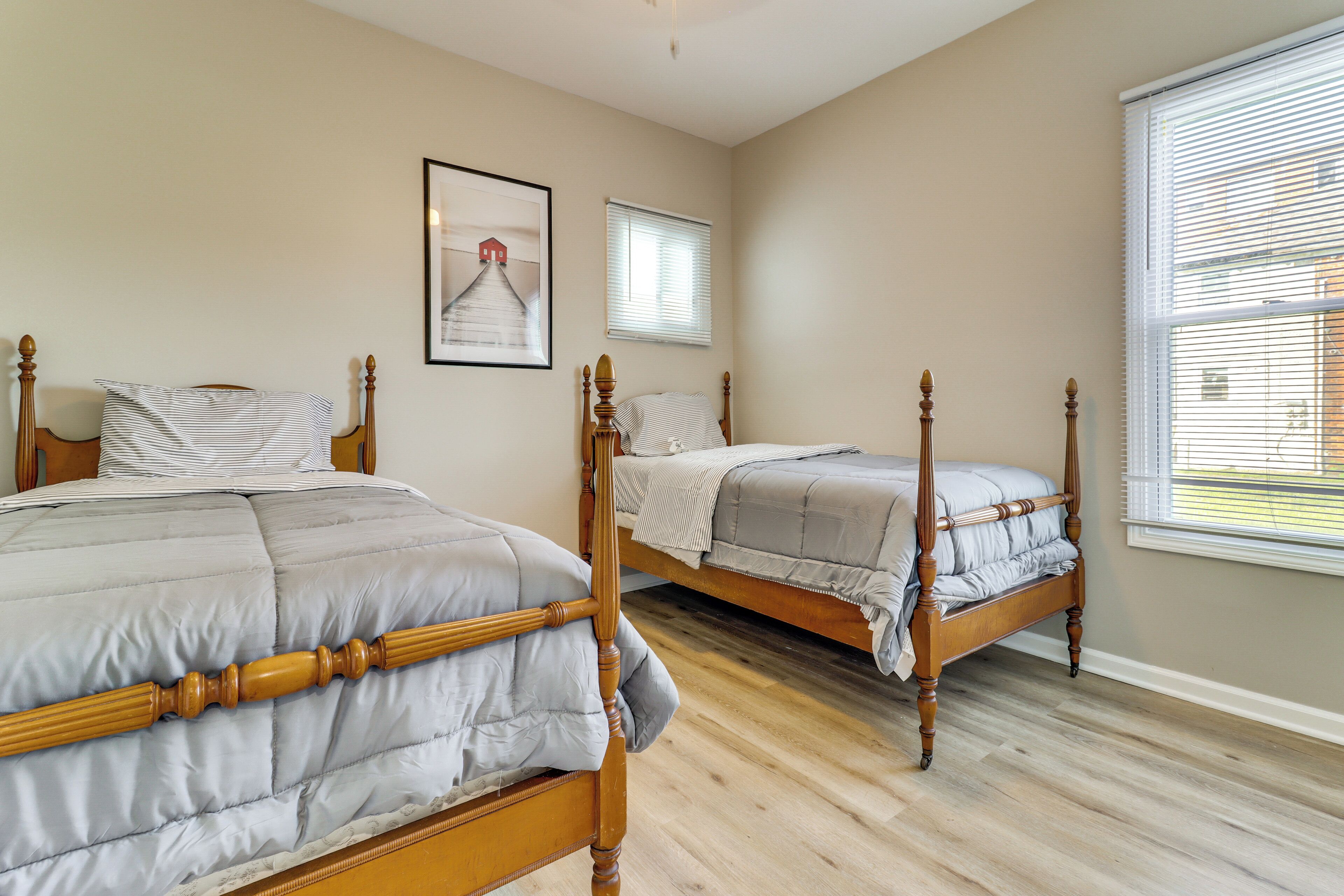 A bedroom with two wooden beds, a framed picture on the wall, and a window with blinds.