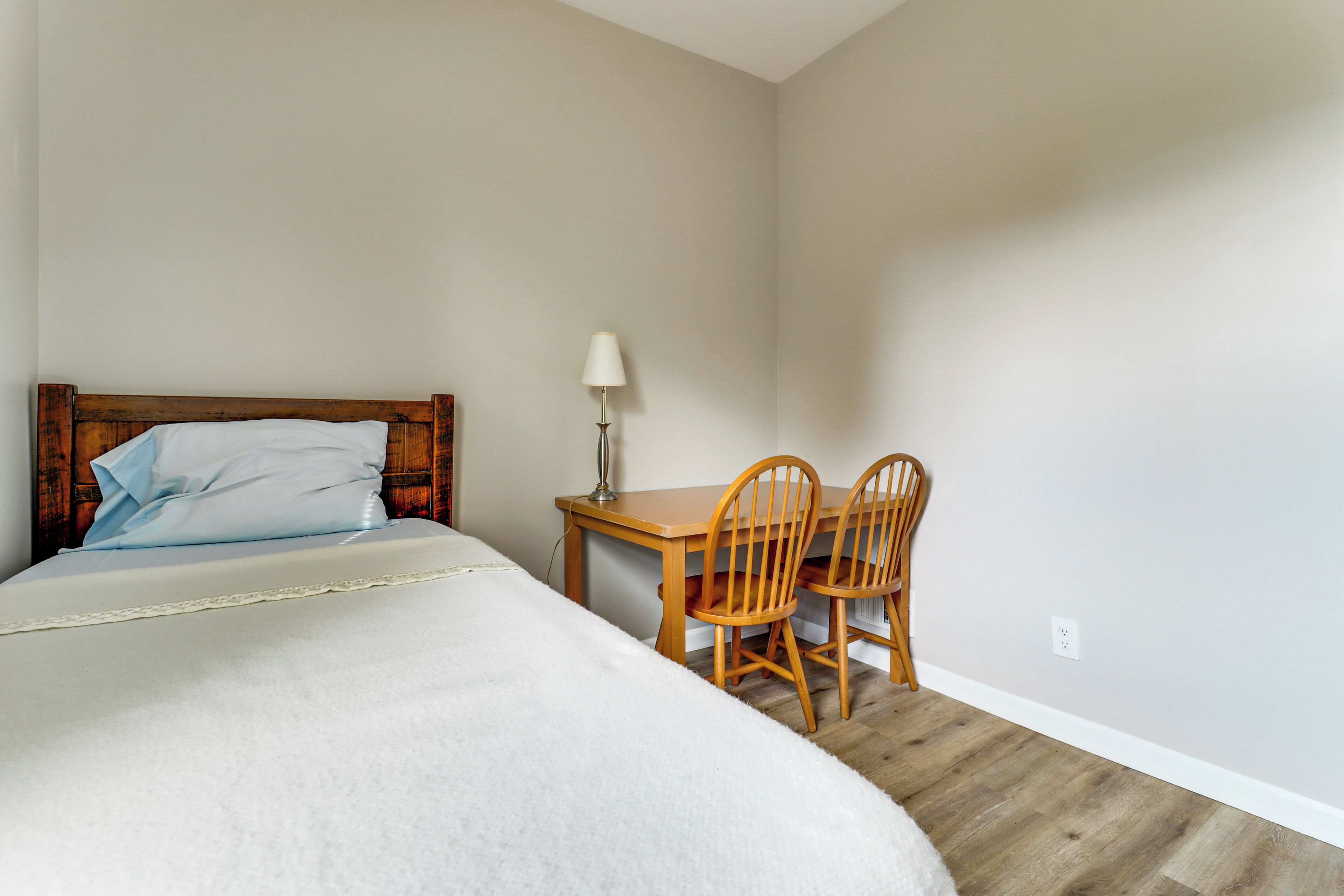 Une chambre à coucher avec un lit, un bureau, deux chaises, une lampe et un plancher en bois.