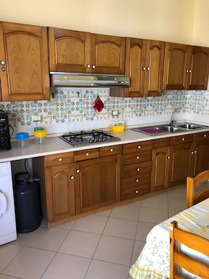 Une cuisine avec des meubles de rangement en bois, une cuisiniÚre à gaz, un évier en acier inoxydable et un crédence décorée.