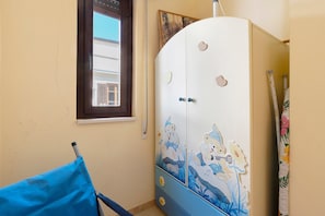 Una habitación con un armario decorado con personajes de caricaturas, una ventana con persianas y una silla azul.