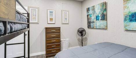 A bedroom with bunk beds, a dresser, a fan, and framed pictures on the wall.