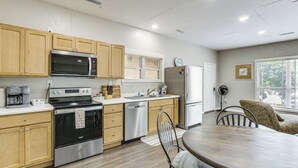 Una cocina moderna con armarios de madera, electrodomésticos de acero inoxidable, una zona de comedor con una mesa redonda y una ventana con persianas.