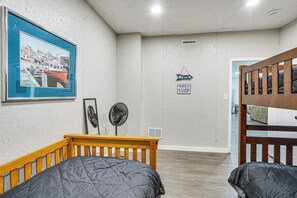 Ein Zimmer mit zwei Betten, einem gerahmten Bild eines Hafens, einem Ventilator und einem Schild mit der Aufschrift 'BEACH'.