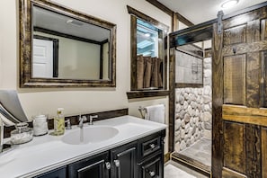 A bathroom with a large mirror, a sink, and a shower area.