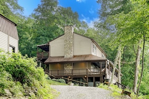 A two-story house with a stone chimney, wooden deck, and a porch.