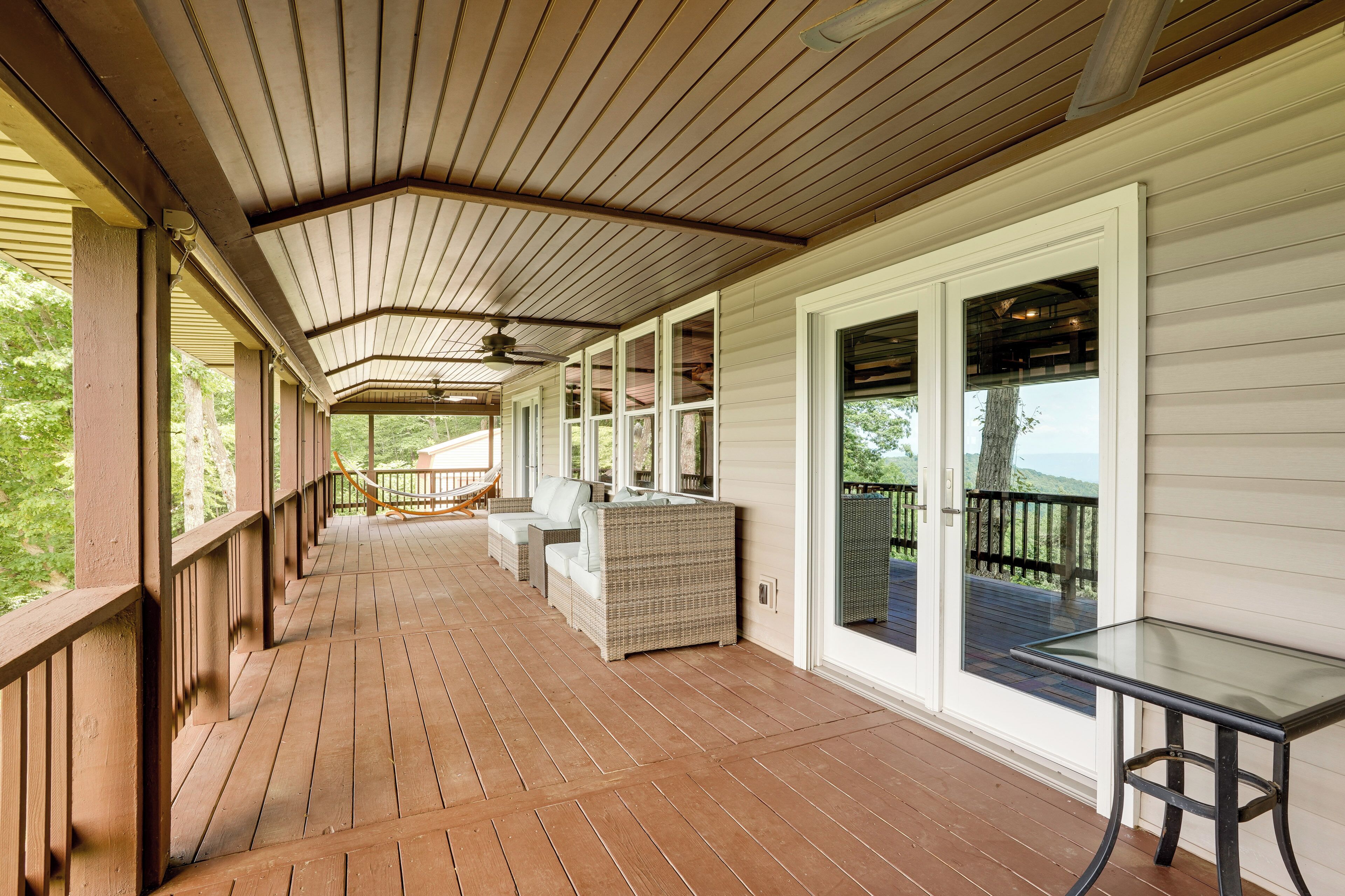 A covered porch with a ceiling fan, a glass table, wicker furniture, and a view of the outdoors.