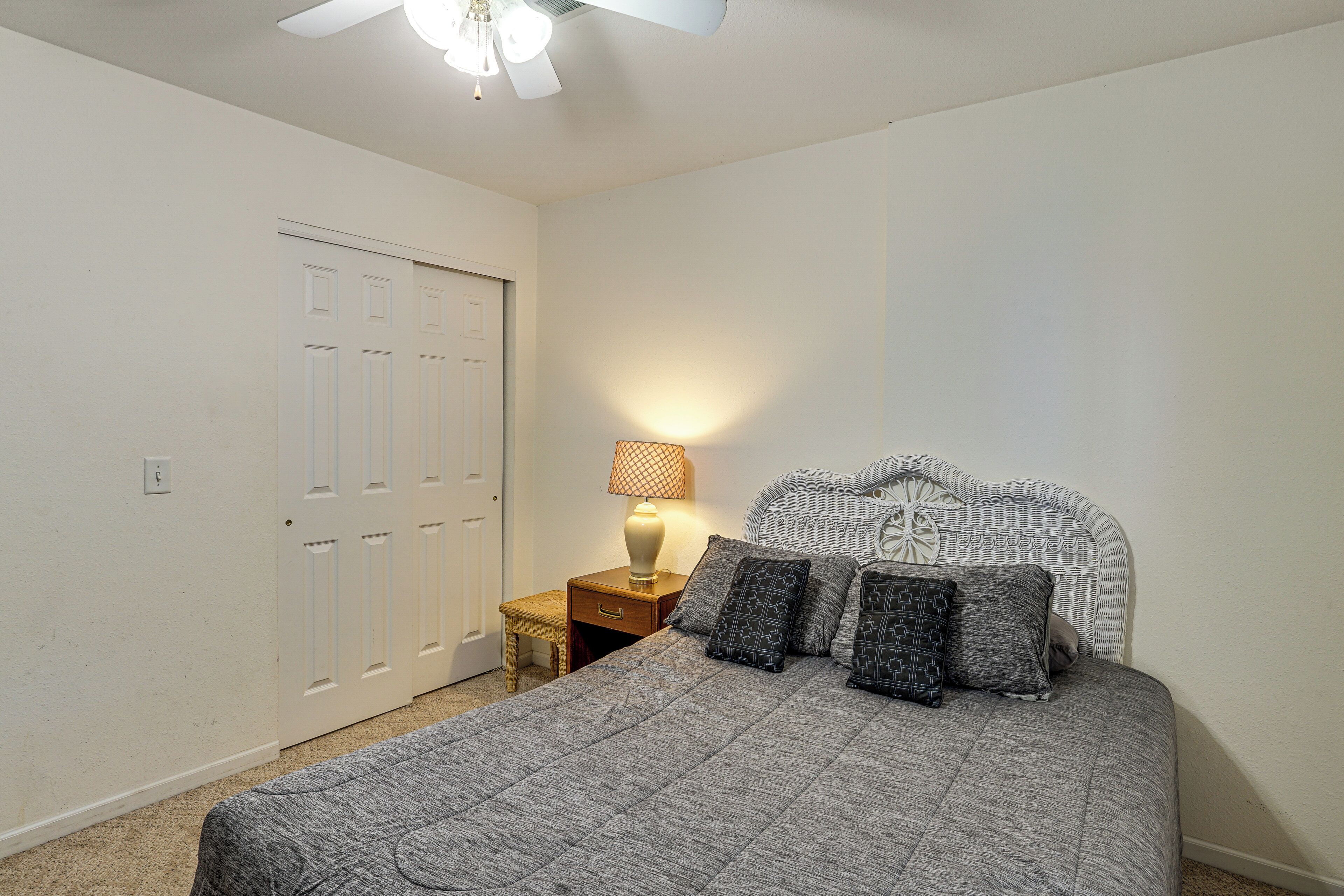 Een slaapkamer met een bed, nachtkastje, lamp en plafondventilator.